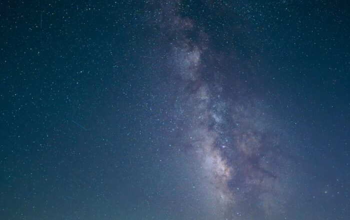 The Milky Way rising above an empty desert highway, its center line vanishing toward distant hills